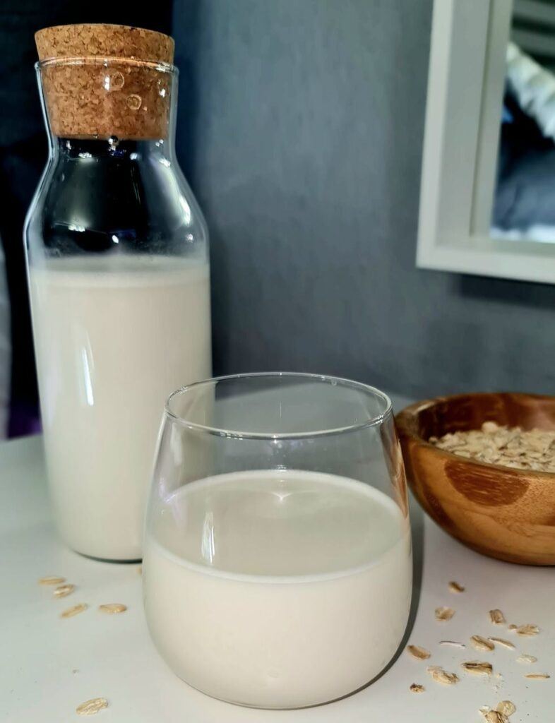 glass and glass bottle with oat milk, a wood bowl with oats and oats on the table.