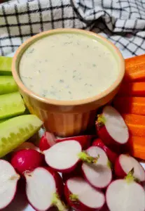 Bowl of vegan ranch dressing surrounded by fresh vegetables.