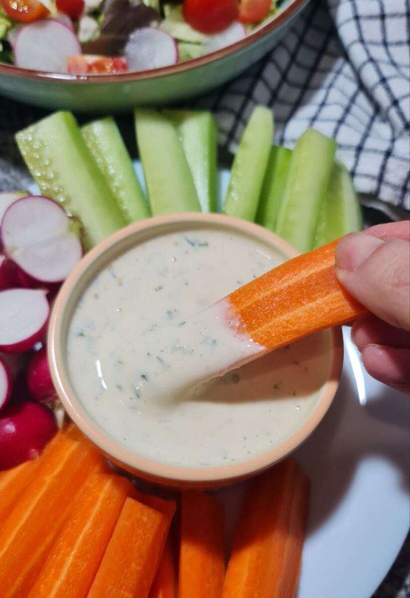 easy vegan ranch dressing recipe. Dipping carrot stick into a bowl of vegan ranch dressing.