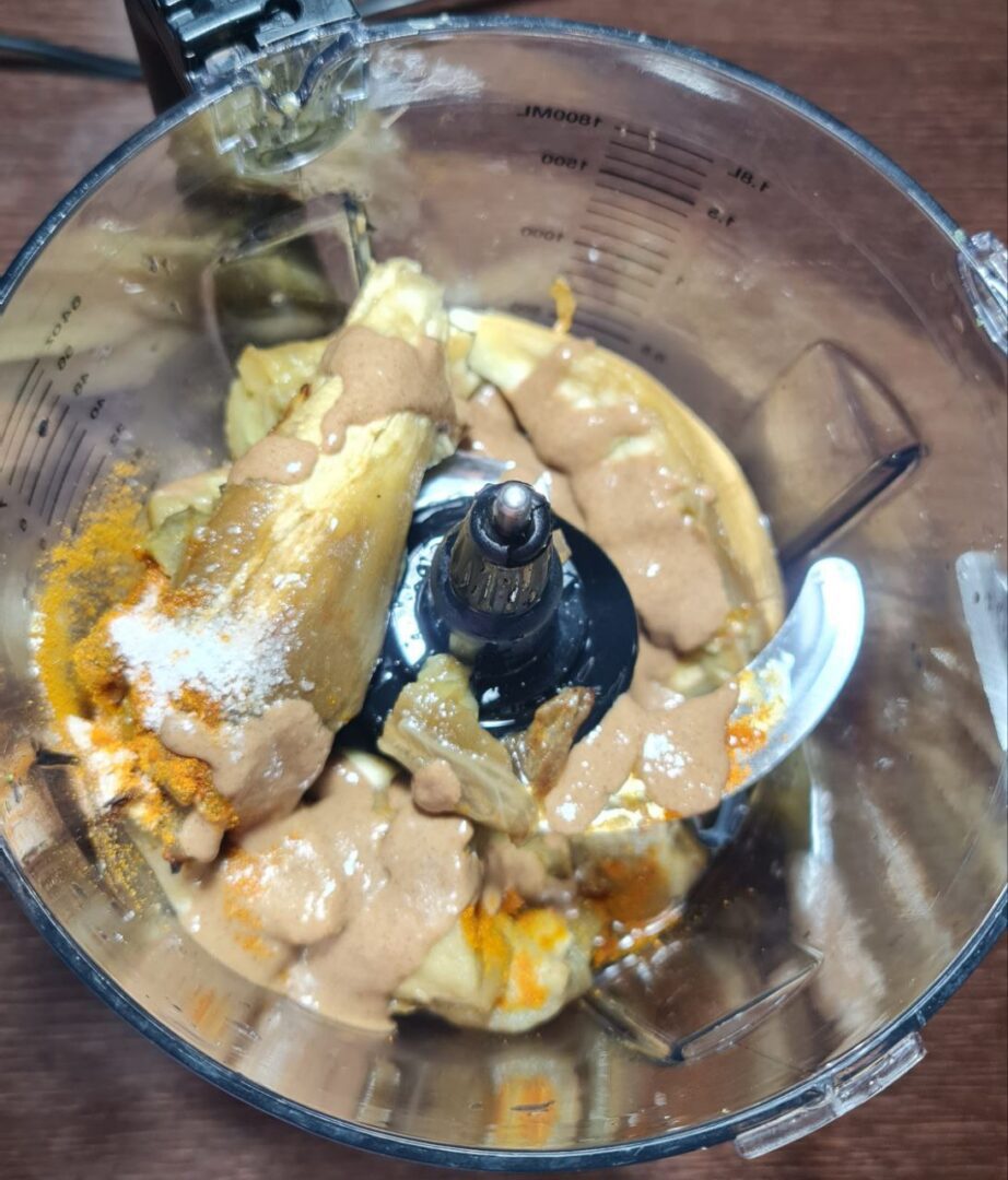 Ingredients for baba ganoush including roasted eggplant, tahini, and turmeric in a blender ready for mixing.