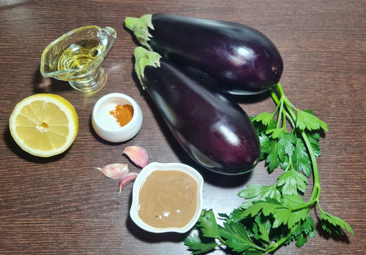 Fresh ingredients for Baba Ganoush recipe on wooden table, including eggplants, olive oil, lemon, garlic, tahini, parsley, and spices.