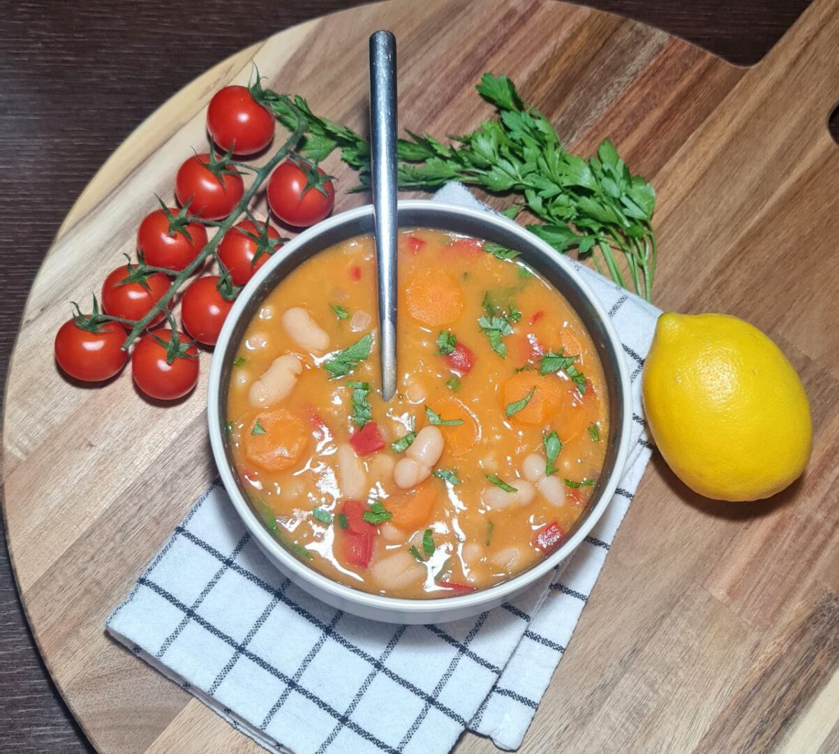 Bowl of creamy bean soup with carrots and herbs, garnished with fresh cherry tomatoes and a lemon.