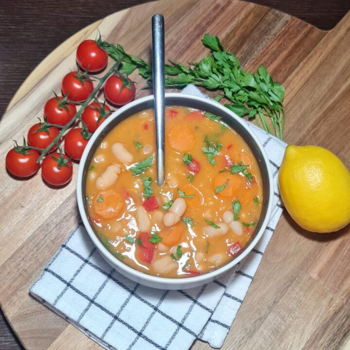 Bowl of creamy bean soup with carrots and herbs, garnished with fresh cherry tomatoes and a lemon.