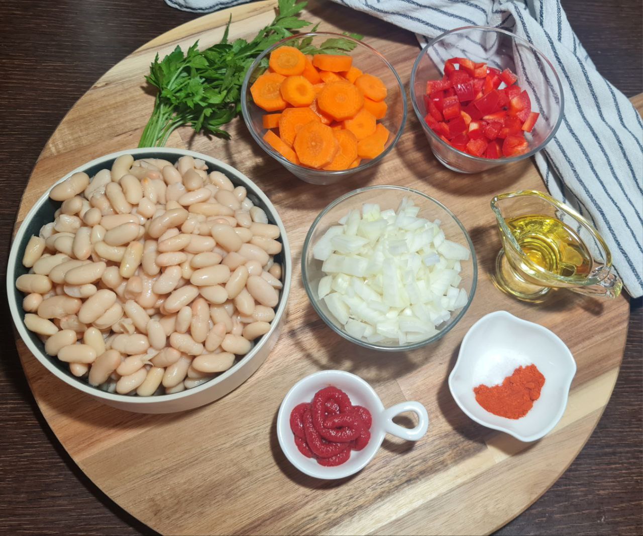 Ingredients for creamy bean soup including white beans, chopped onions, carrots, red bell peppers, tomato paste, olive oil, and spices.