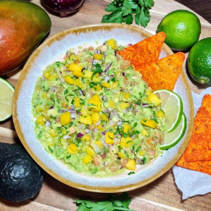 Fresh mango guacamole garnished with red onion, cilantro, and lime wedges, served with tortilla chips.