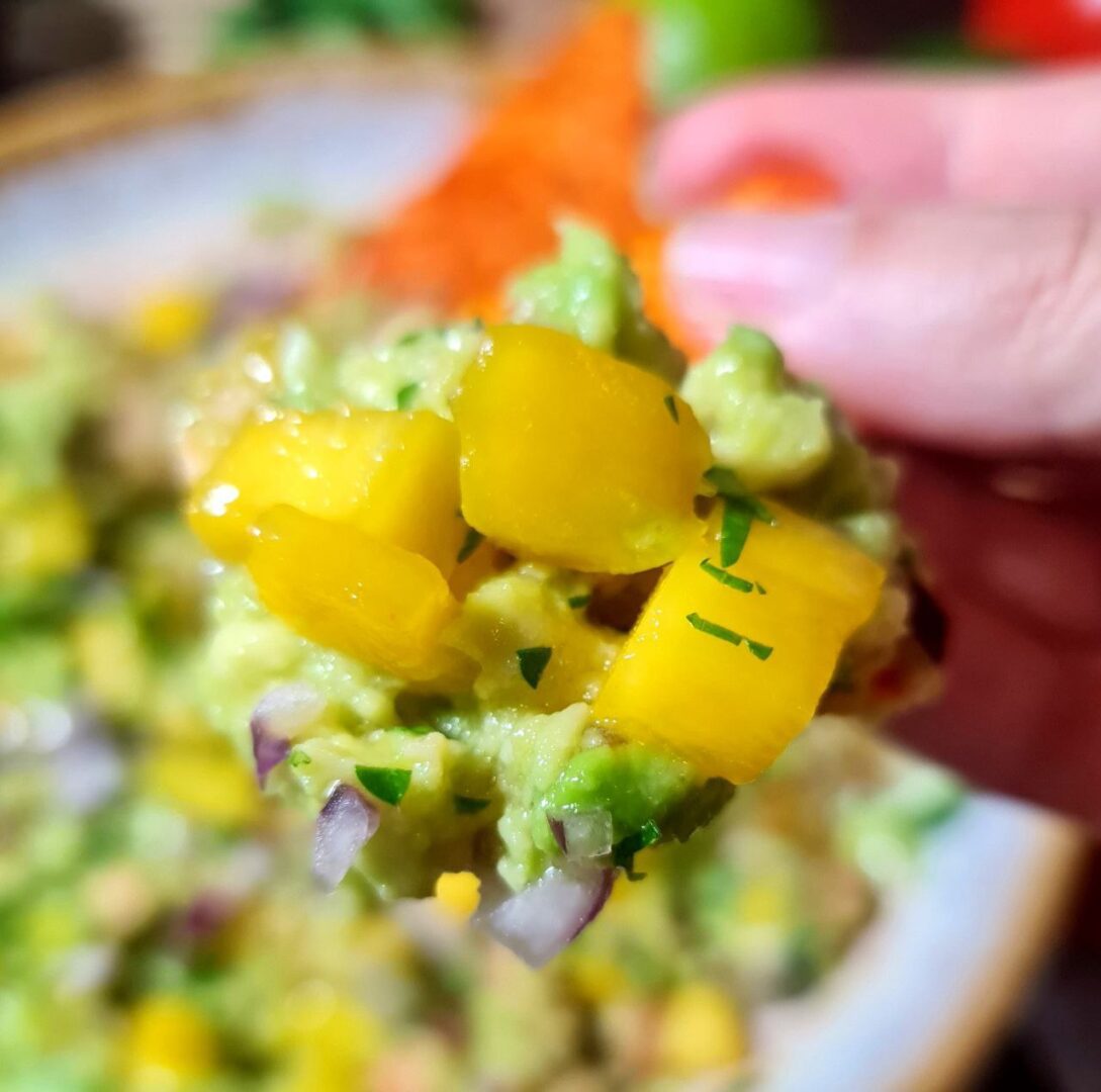 Close-up of mango guacamole on a tortilla chip showing chunks of mango, avocado, red onion, and cilantro.