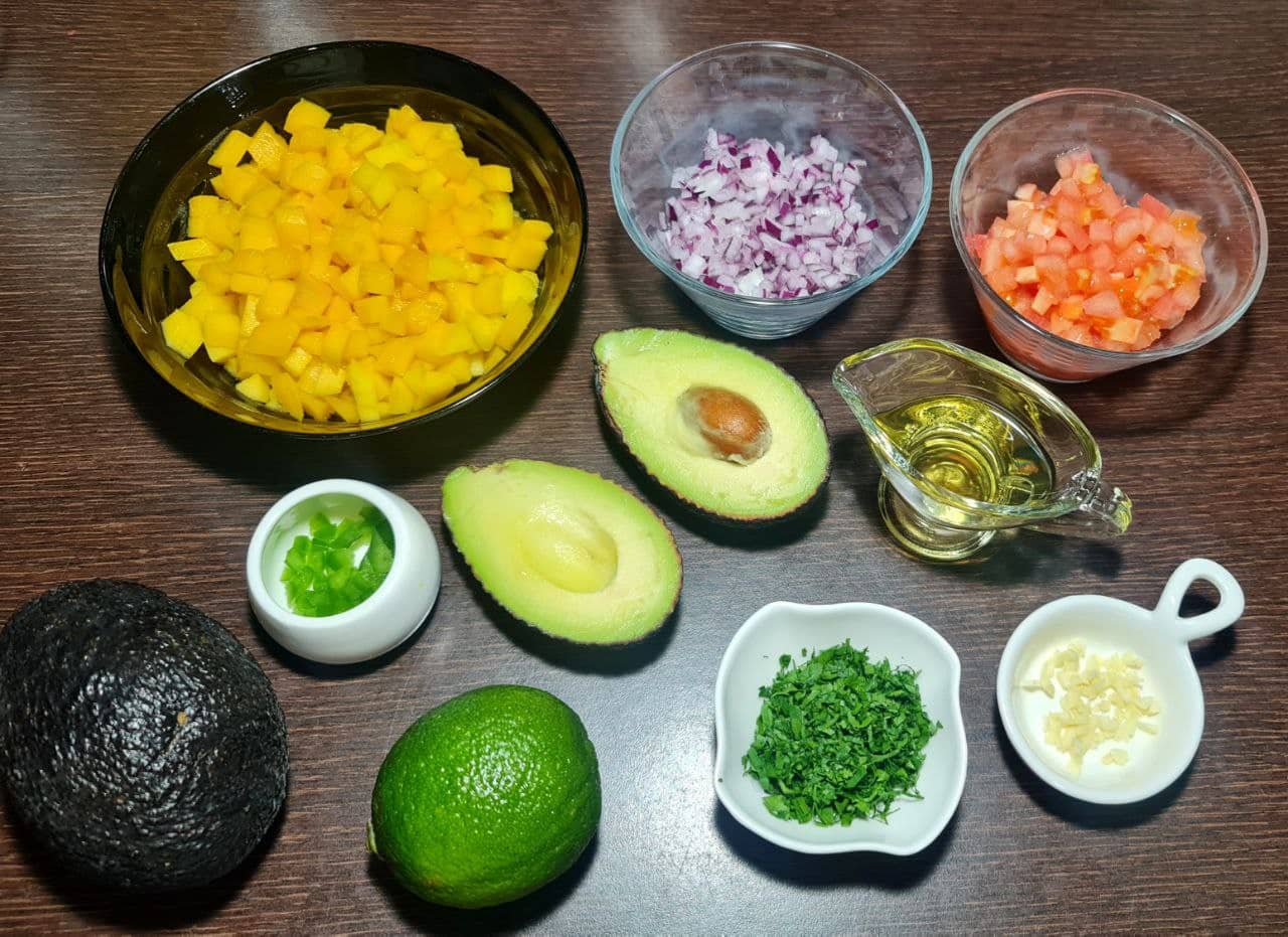 Ingredients for mango guacamole including diced mango, avocado, red onion, tomato, cilantro, lime, garlic, jalapeno, and olive oil.