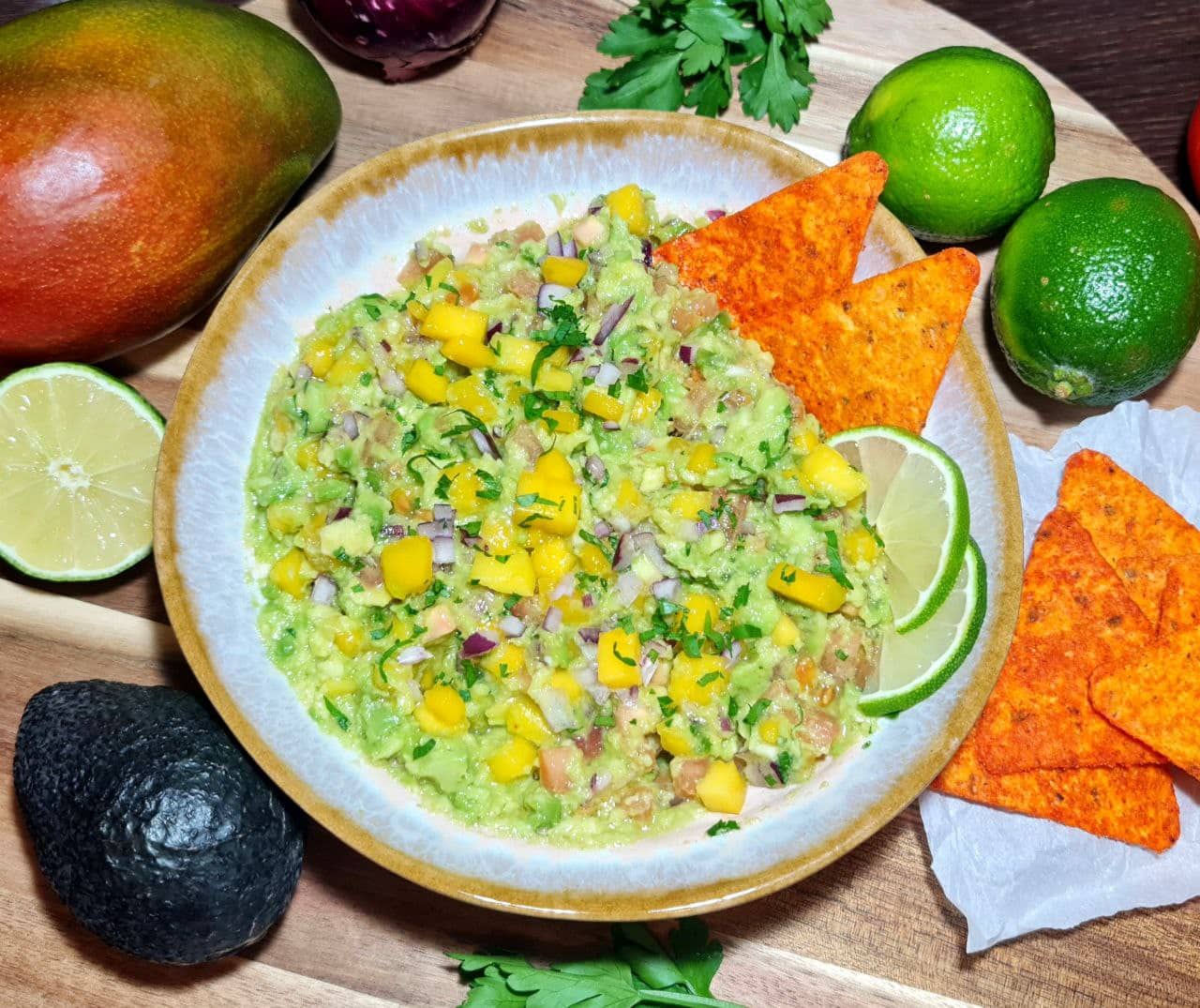 Fresh mango guacamole garnished with red onion, cilantro, and lime wedges, served with tortilla chips.