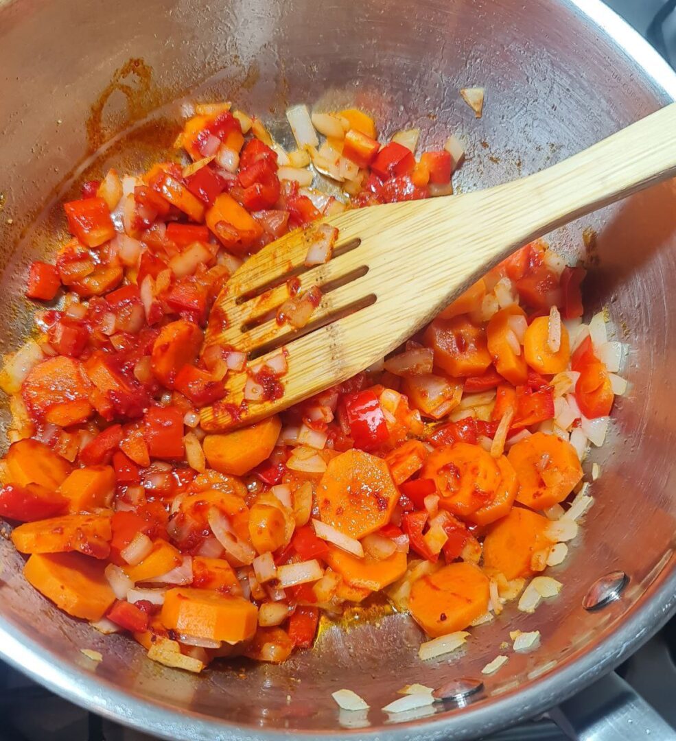 Sautéing vegetables for creamy bean soup including carrots, red bell peppers, and onions in a pot.