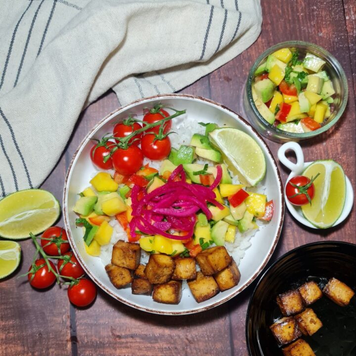 A vibrant tropical tofu rice bowl with pickled onions, mango salsa, avocado, cherry tomatoes, and crispy tofu cubes served on a bed of white rice.