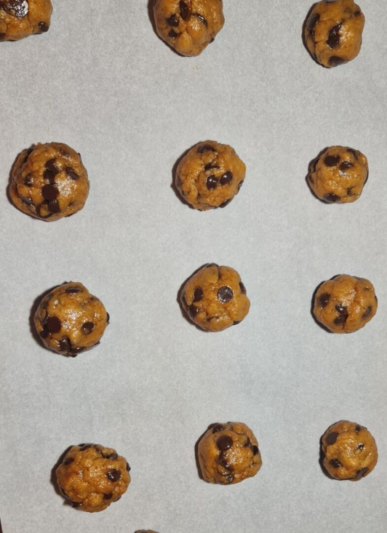 Unbaked balls of vegan chocolate chip cookie dough on parchment paper, evenly spaced to allow for baking expansion.