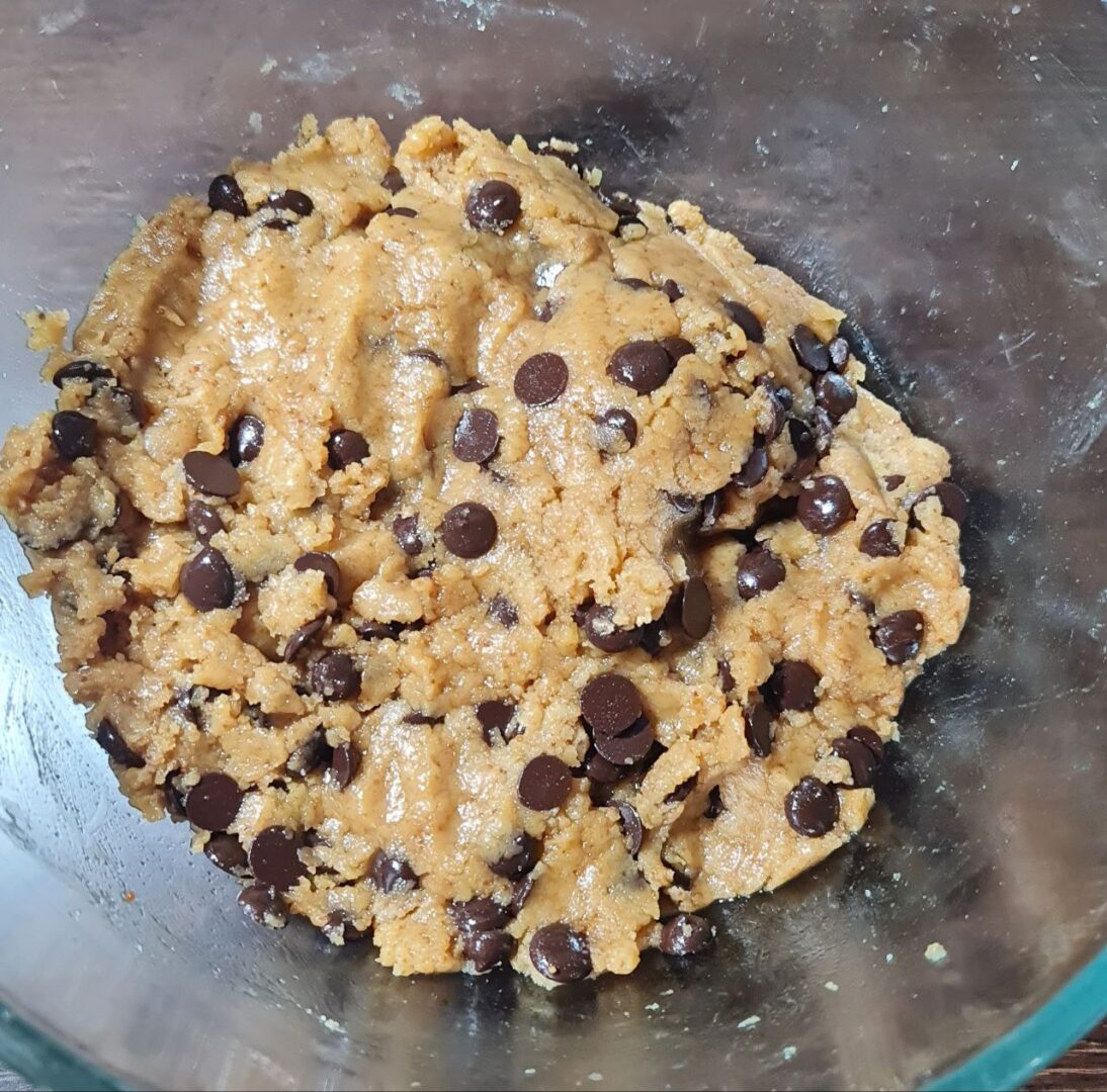 Close-up of vegan chocolate chip cookie dough in a mixing bowl, richly studded with dark chocolate chips.