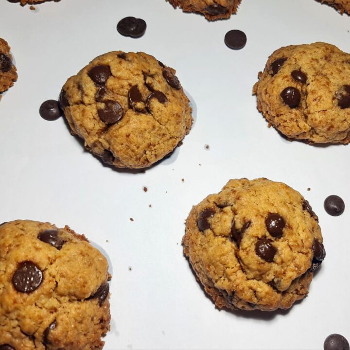 Freshly baked vegan chocolate chip cookies on a white background, scattered with extra chocolate chips