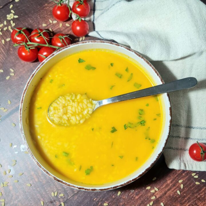 Vibrant vegan pastina soup in a rustic bowl, garnished with fresh parsley, served alongside cherry tomatoes on a wooden surface.