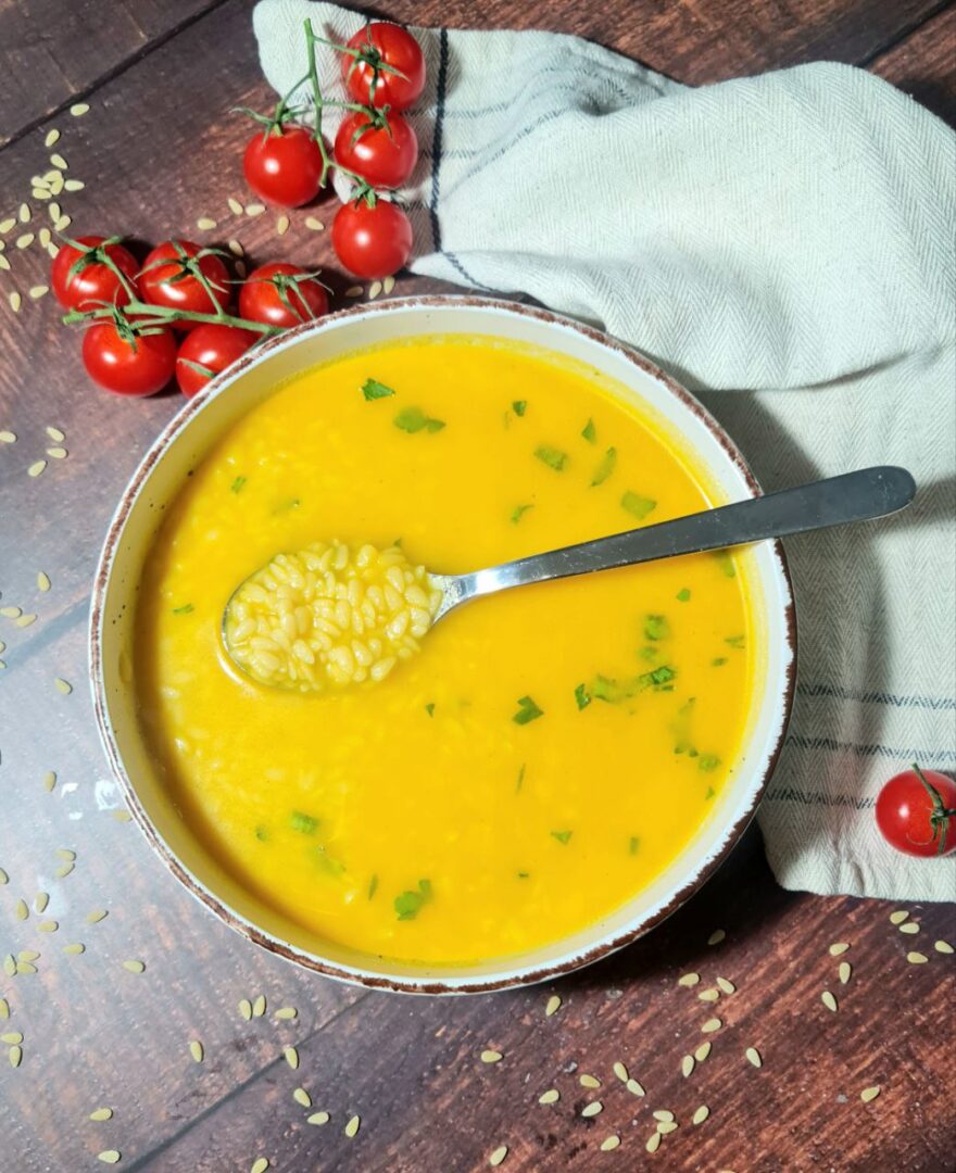 Vibrant vegan pastina soup in a rustic bowl, garnished with fresh parsley, served alongside cherry tomatoes on a wooden surface.