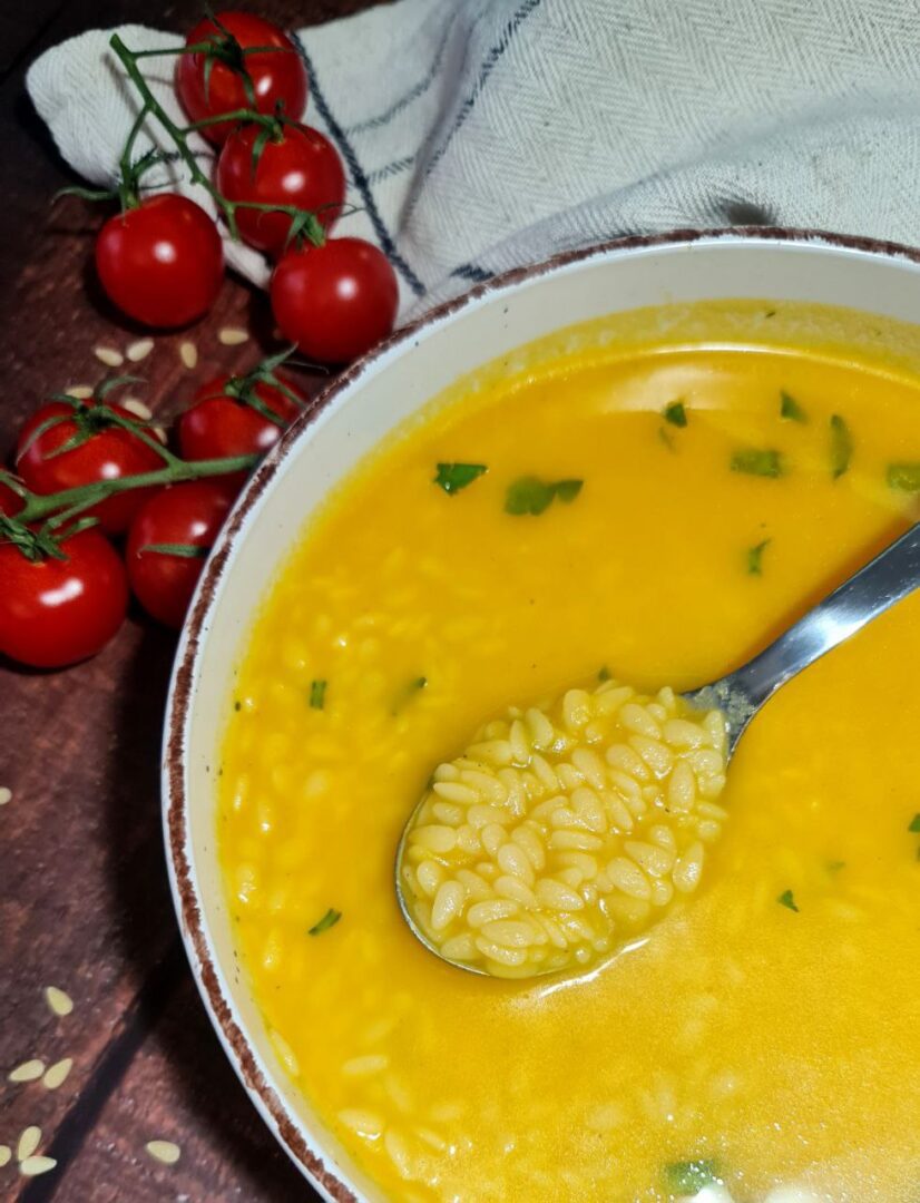 A bowl of vibrant vegan pastina soup garnished with fresh herbs, alongside ripe cherry tomatoes, emphasizing a healthy plant-based meal.