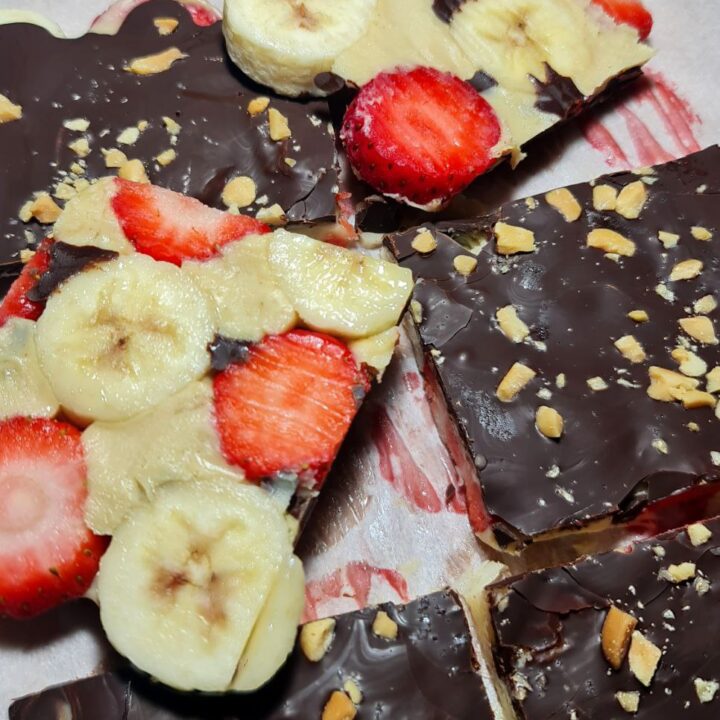 Closeup of banana strawberry chocolate peanut butter bark showing layers of dark chocolate, peanut butter, banana slices, strawberries, and crushed nuts.