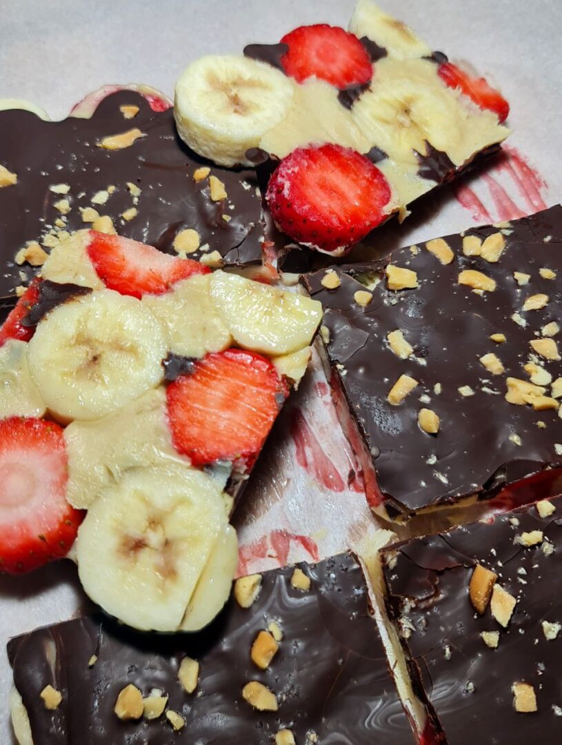 Closeup of banana strawberry chocolate peanut butter bark showing layers of dark chocolate, peanut butter, banana slices, strawberries, and crushed nuts.