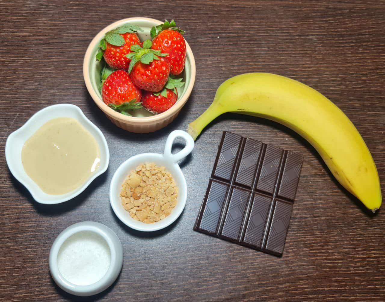 Ingredients for banana strawberry chocolate peanut butter bark including banana, strawberries, dark chocolate, peanut butter, crushed nuts, and coconut flakes.