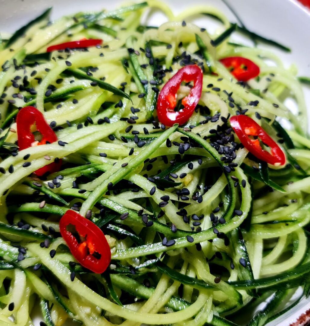  Close-up view of a cucumber noodle salad garnished with black sesame seeds and red chili slices.