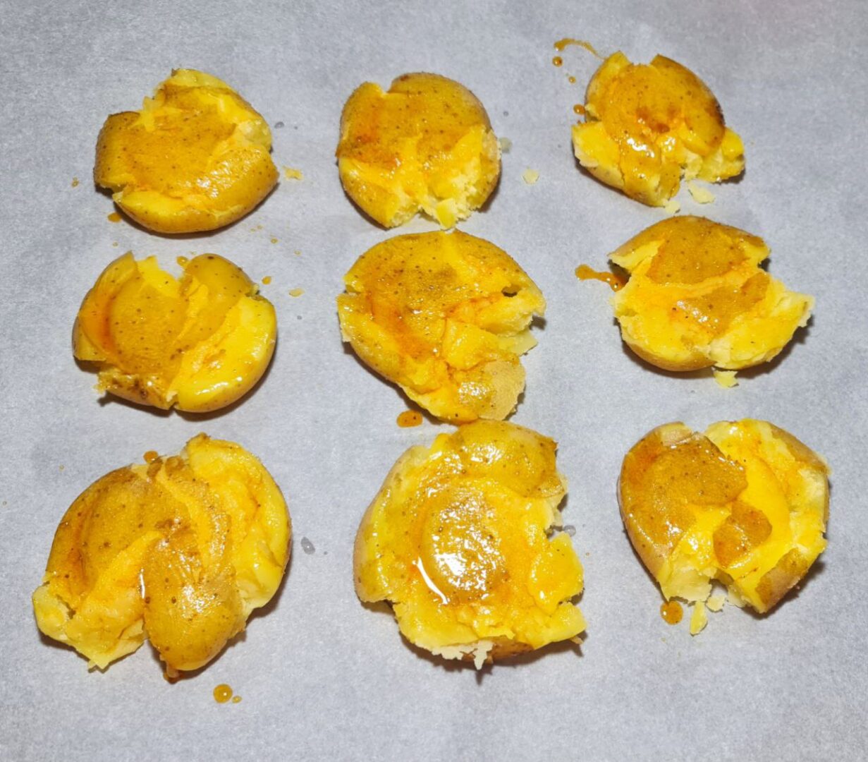 Partially smashed potatoes seasoned and ready to be baked.Caption: Partially smashed potatoes seasoned with spices, ready for baking