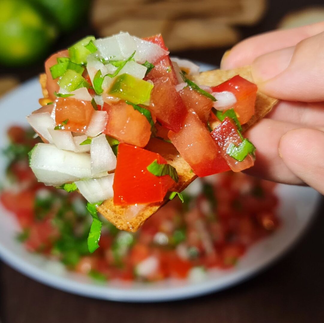  A close-up of a hand holding a tortilla chip topped with fresh pico de gallo.