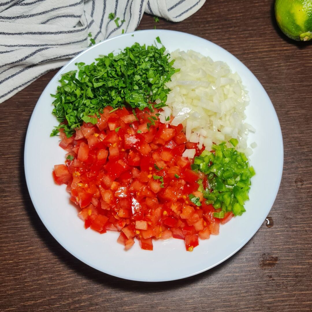  Freshly chopped ingredients for pico de gallo on a white plate, including tomatoes, onions, cilantro, and jalapeños.