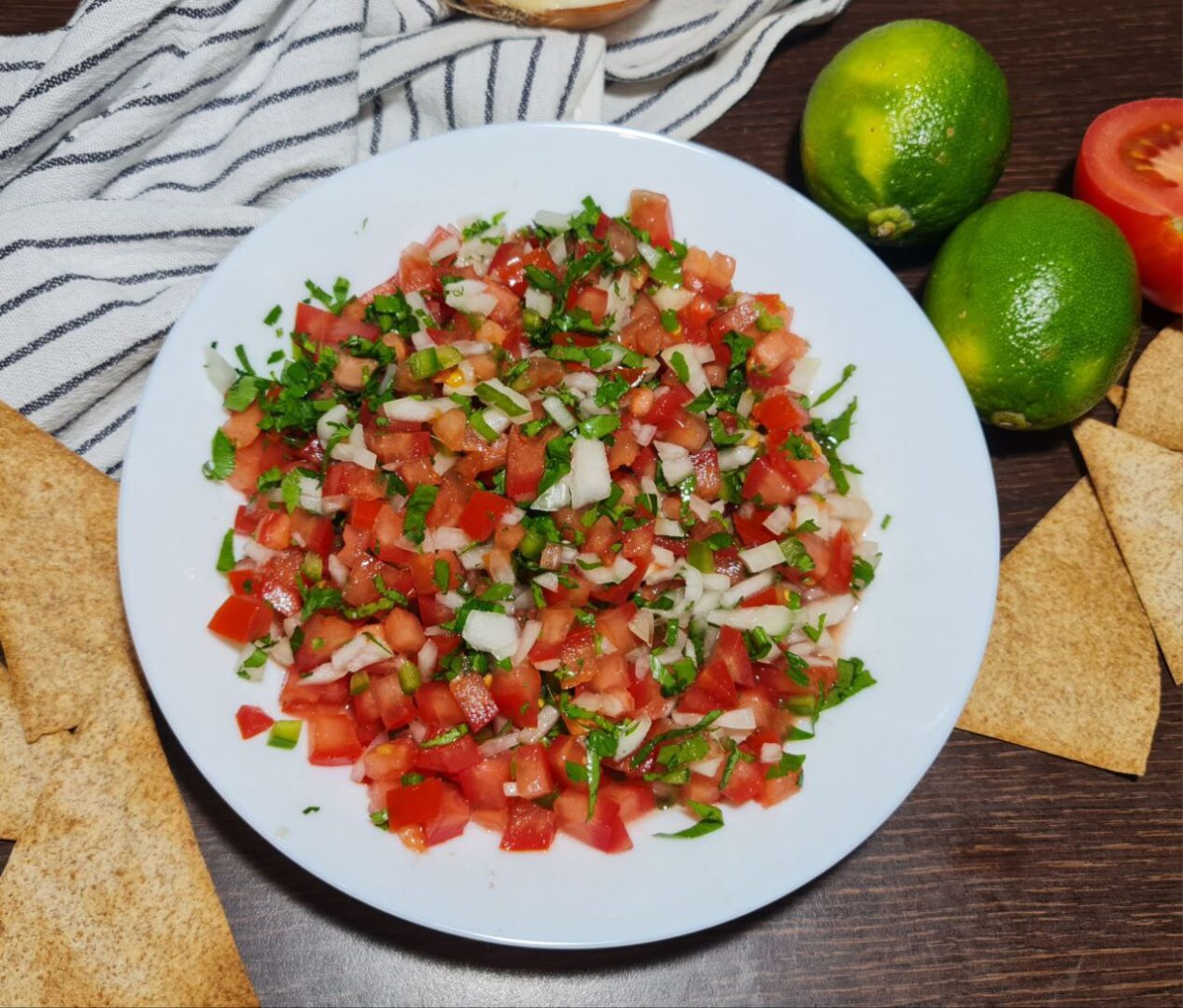 Fresh homemade pico de gallo served with tortilla chips, limes, and a tomato.