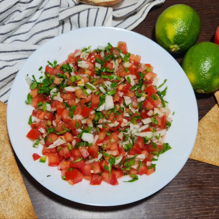 Fresh homemade pico de gallo served with tortilla chips, limes, and a tomato.