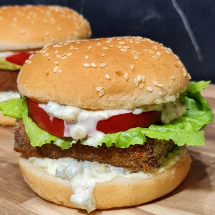 A delicious vegan tofu burger with lettuce, tomato, and creamy sauce in a sesame seed bun.