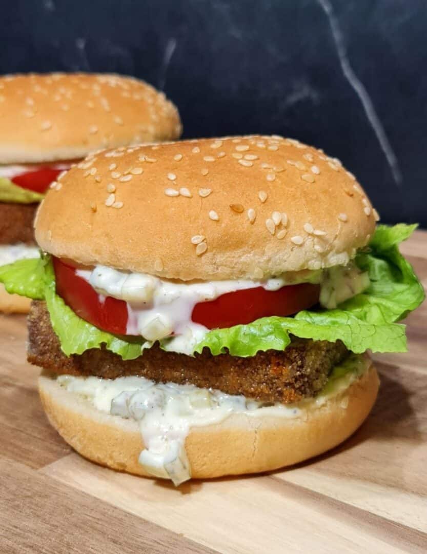 A delicious vegan tofu burger with lettuce, tomato, and creamy sauce in a sesame seed bun.