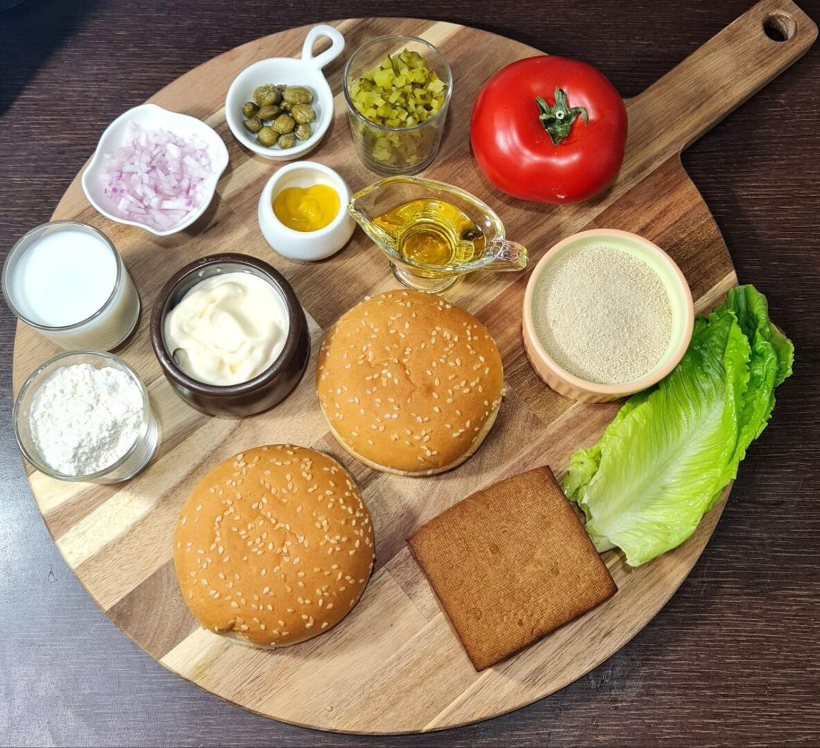 Ingredients for making the best vegan tofu burger including tofu, lettuce, tomato, buns, and various condiments arranged on a wooden board.