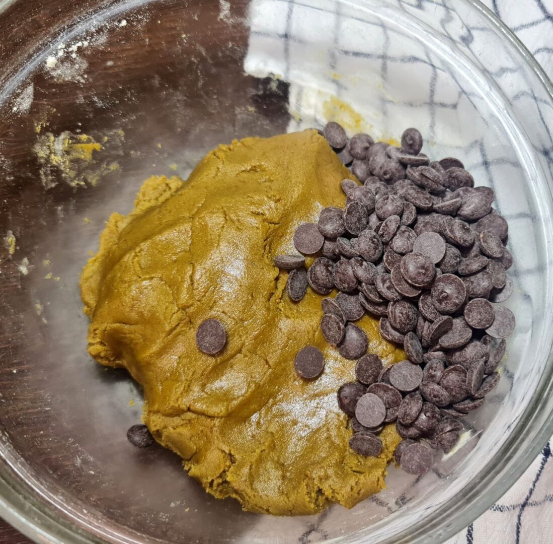  Vegan matcha cookie dough in a glass bowl with chocolate chips ready to be mixed in.