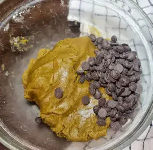 Vegan matcha cookie dough in a glass bowl with chocolate chips ready to be mixed in.