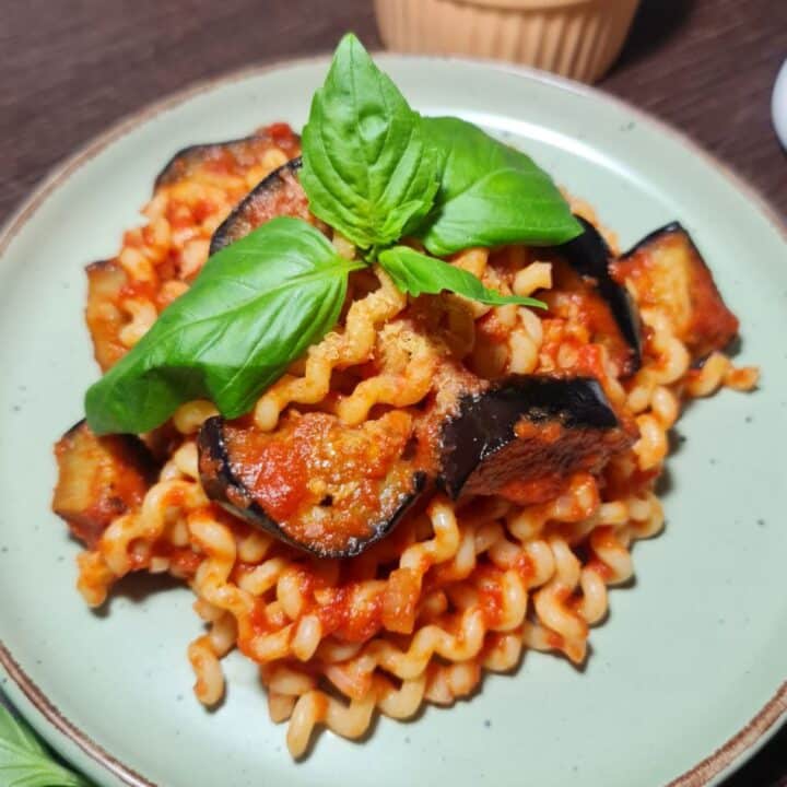 A plate of vegan Pasta alla Norma garnished with fresh basil leaves.