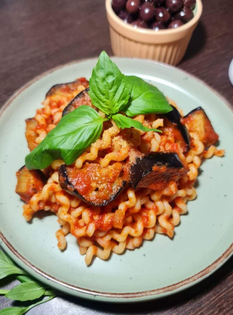 A plate of vegan Pasta alla Norma garnished with fresh basil leaves.