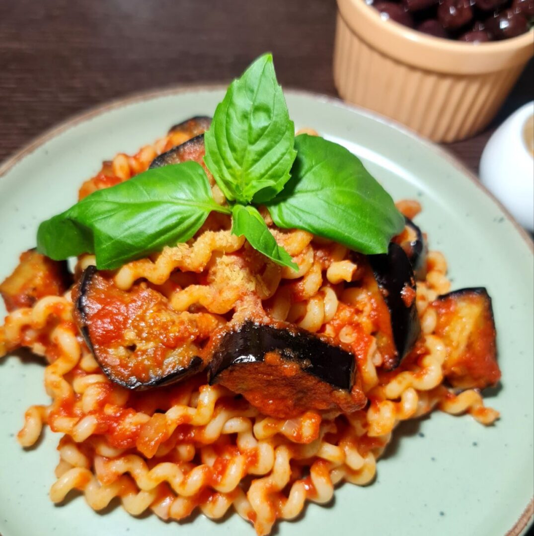 Close-up of vegan Pasta alla Norma topped with fresh basil leaves on a green plate.