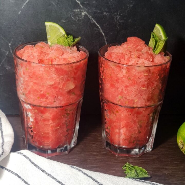 Two glasses of refreshing watermelon slushie garnished with lime wedges and mint leaves, with whole and cut limes beside them.