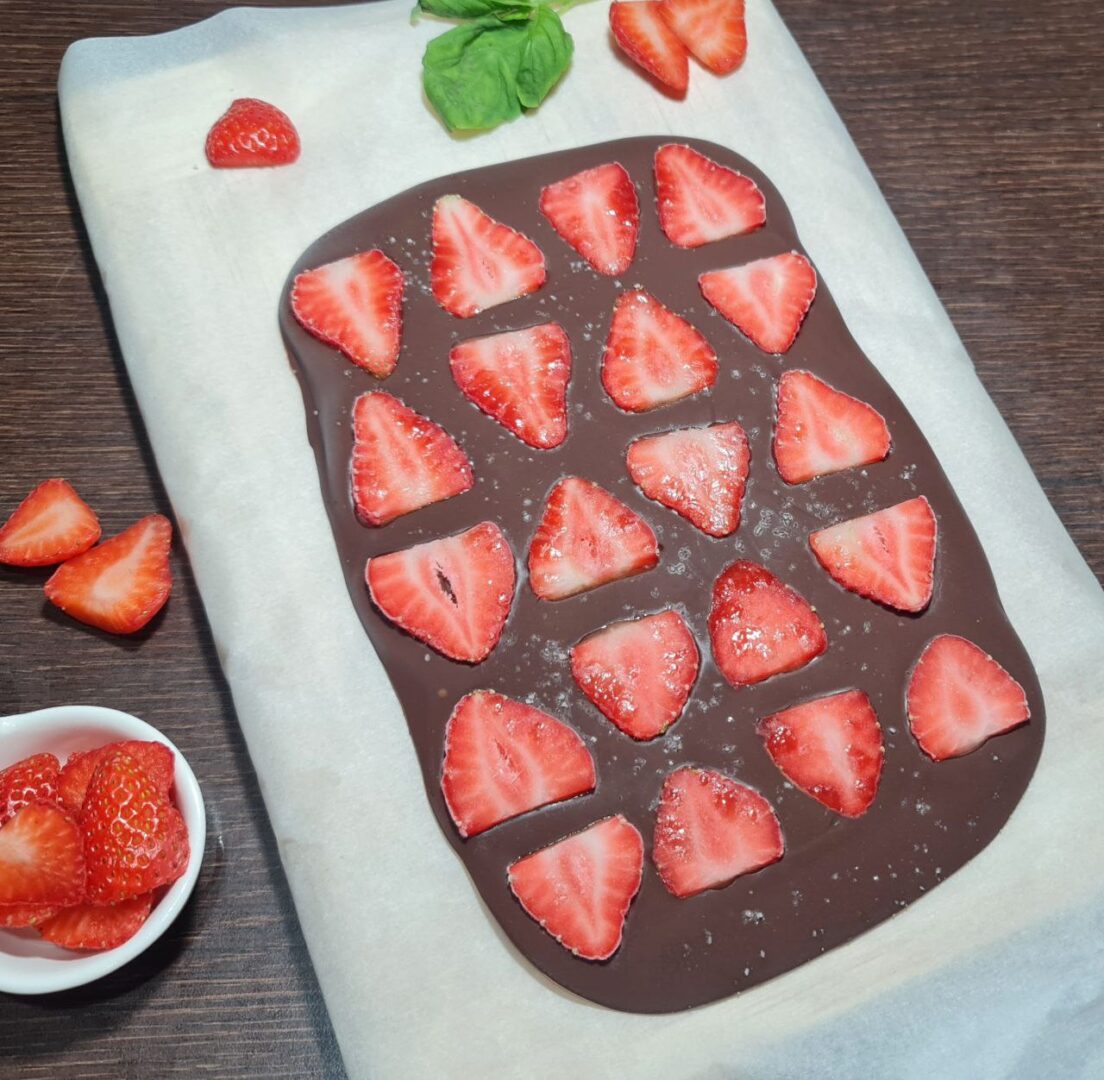  Chocolate peanut butter strawberry bark being prepared on parchment paper with fresh strawberry slices on top. Preparing chocolate peanut butter strawberry bark with fresh strawberry slices, ready to be chilled.