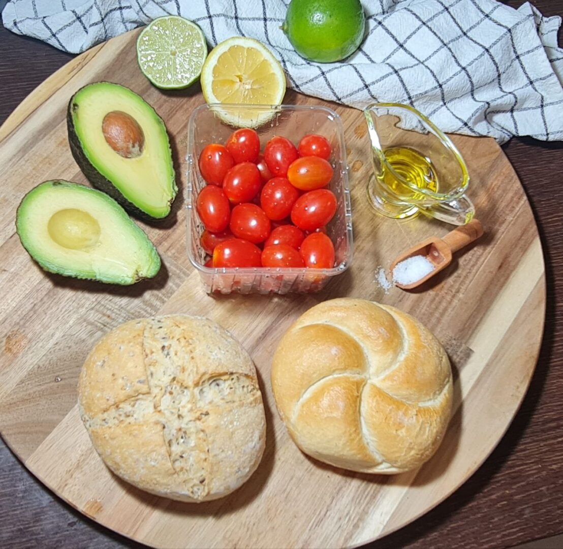  Ingredients for vegan avocado toast including avocado, cherry tomatoes, lime, fresh basil, and sea salt.  Fresh ingredients for making vegan avocado toast: avocado, cherry tomatoes, lime, basil, and sea salt.