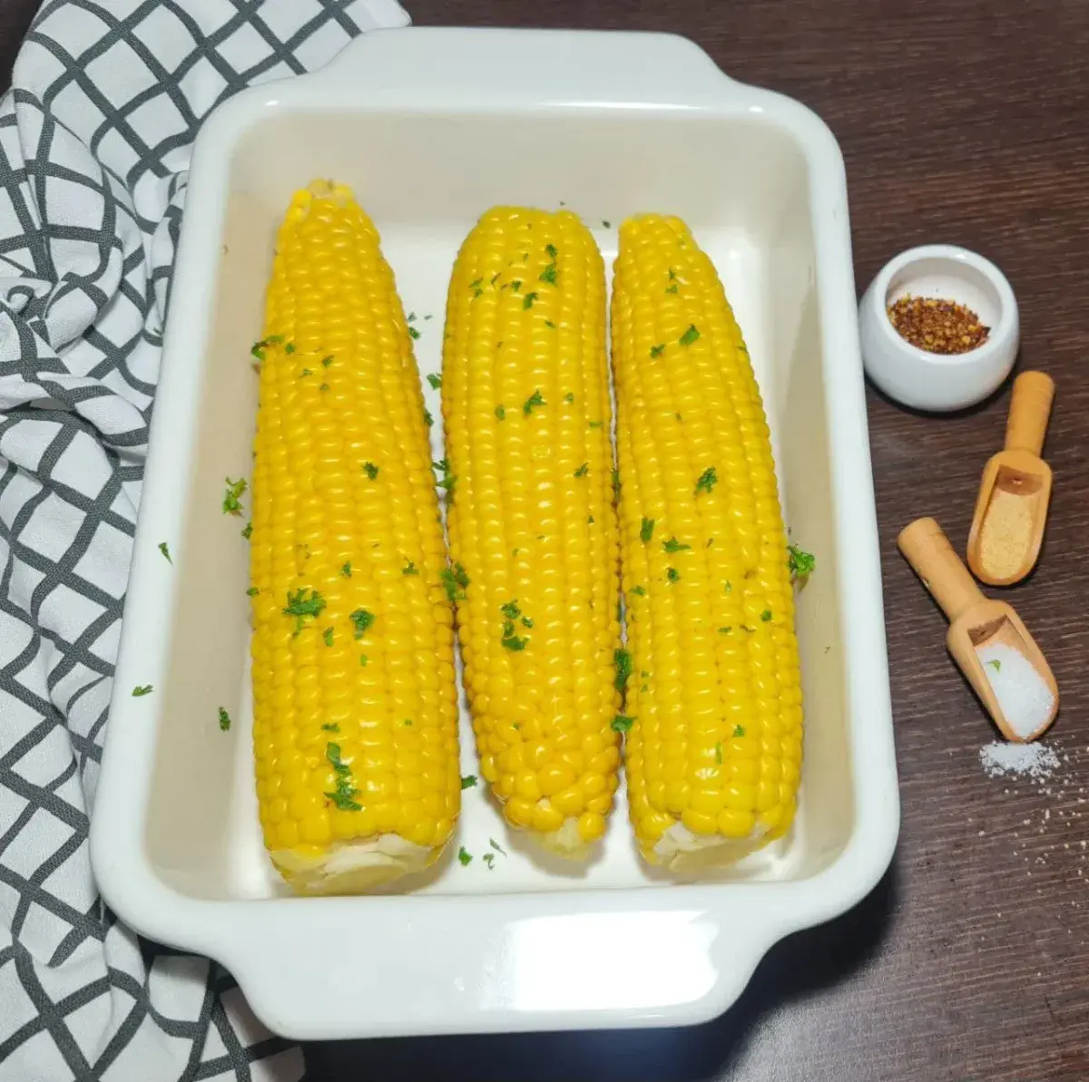 How long to boil corn on the cob. Fresh boiled corn on the cob garnished with parsley in a white baking dish