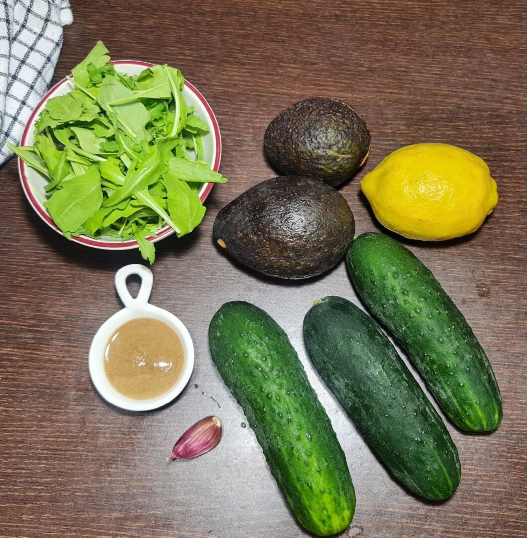 Ingredients for easy cold avocado cucumber soup including arugula, avocados, lemon, cucumbers, garlic, and tahini.