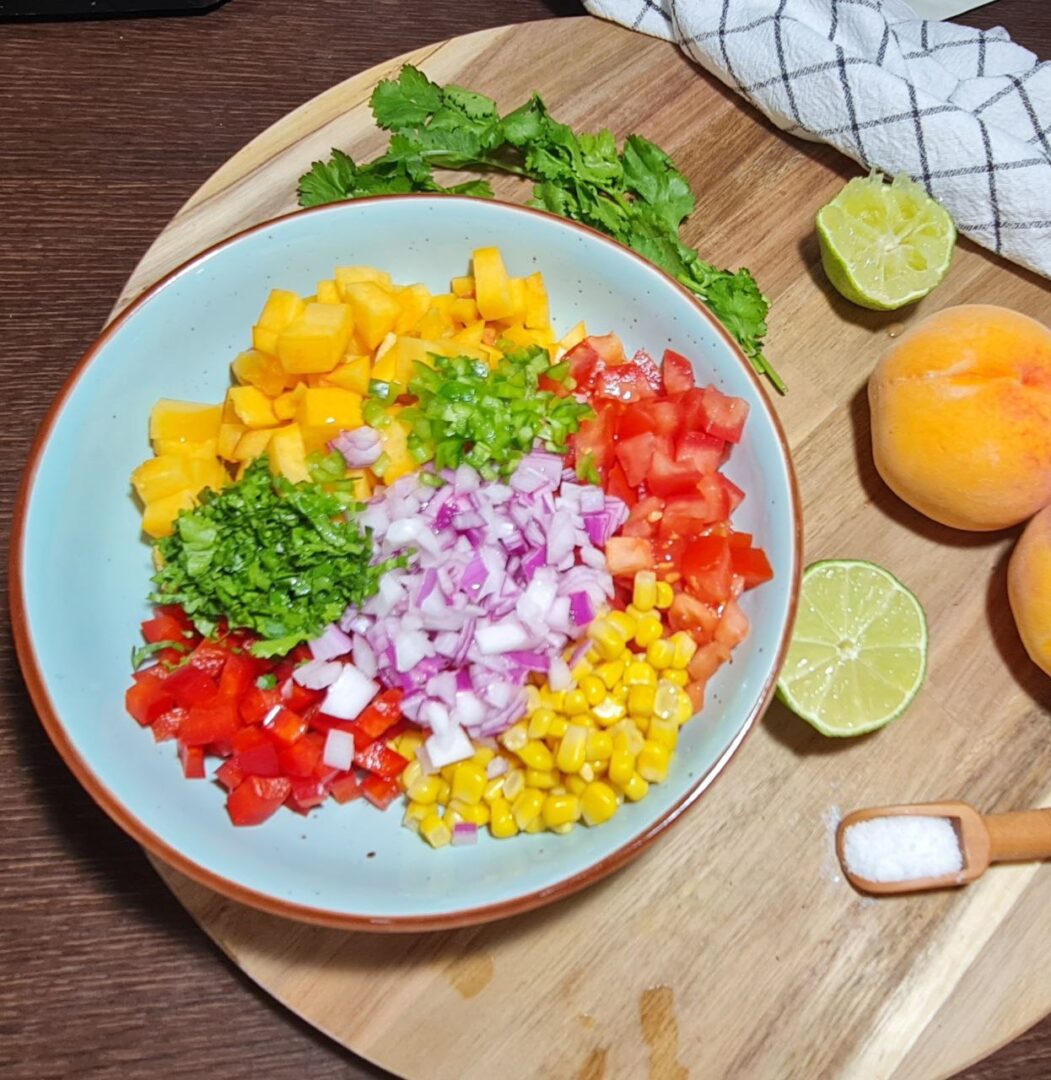  Bowl of diced ingredients for peach salsa, including peaches, red bell pepper, tomatoes, red onion, cilantro, corn, and lime.