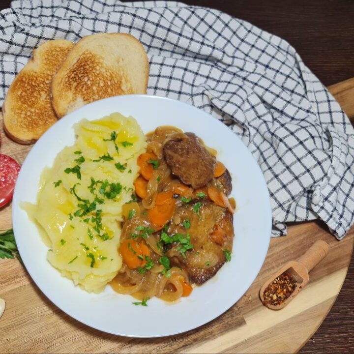 Plate of savory seitan with wine sauce, mashed potatoes, toasted bread, and fresh tomatoes. :A delicious meal of savory seitan with wine sauce served with mashed potatoes, toasted bread, and fresh tomatoes.