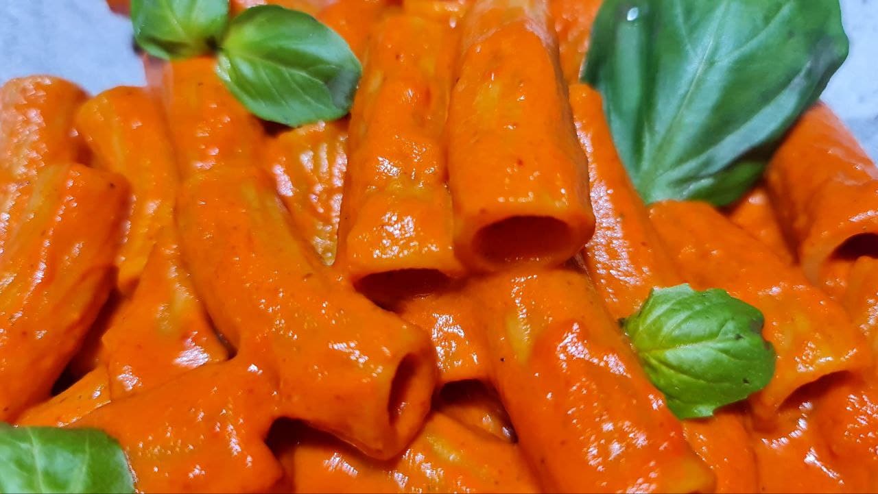 Close-up of creamy rigatoni pasta coated in roasted red pepper sauce, garnished with fresh basil leaves. A detailed close-up of rigatoni pasta coated in a velvety roasted red pepper sauce, with fresh basil adding a burst of color.