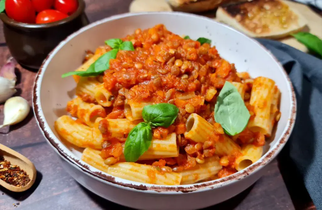 A bowl of rigatoni pasta topped with lentil vegan Bolognese sauce and garnished with basil. Rigatoni pasta served with a generous portion of lentil vegan Bolognese sauce.