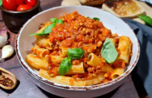 A bowl of rigatoni pasta topped with lentil vegan Bolognese sauce and garnished with basil. Rigatoni pasta served with a generous portion of lentil vegan Bolognese sauce.
