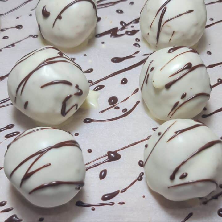 White chocolate-covered truffles on parchment paper, drizzled with dark chocolate.