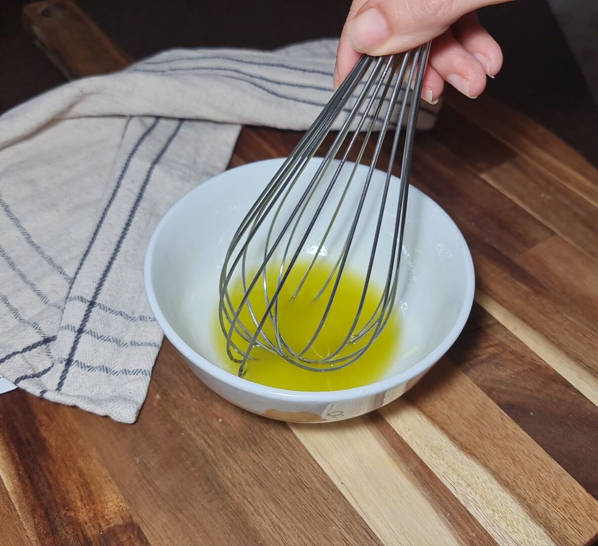 a hand holding a whisk over a bowl of liquid