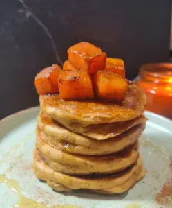 A stack of vegan pumpkin pancakes topped with cinnamon-spiced sweet potato cubes. Fluffy vegan pumpkin pancakes topped with spiced sweet potato cubes.